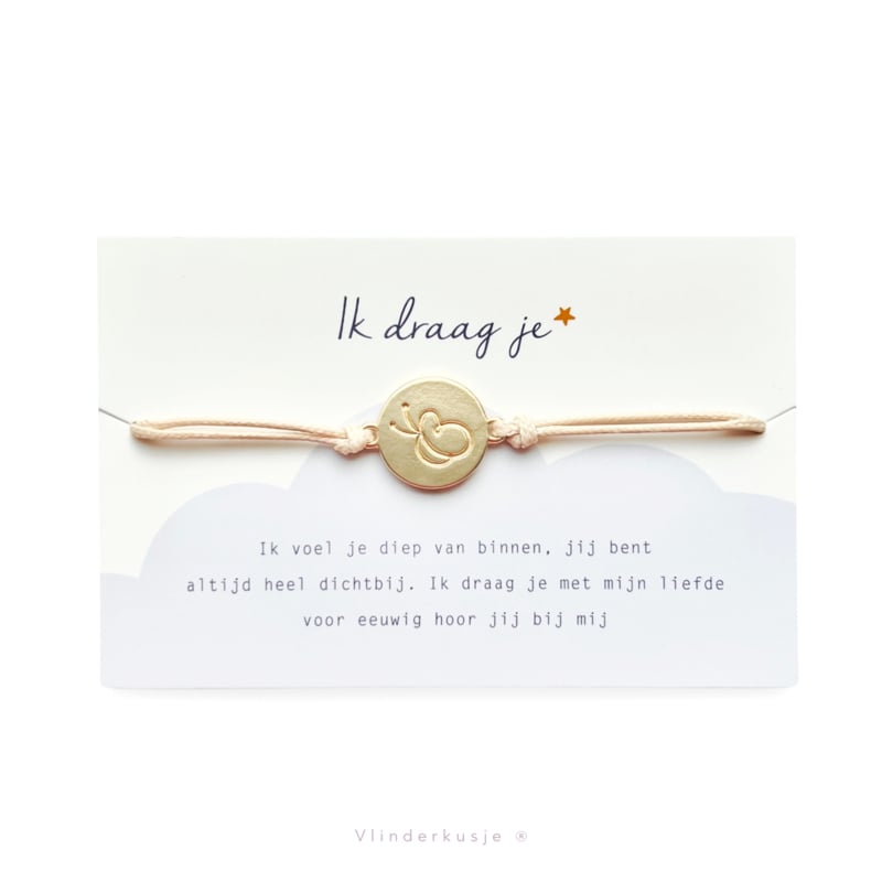 Armbandje Ik Draag Je met lichtroze koord en goudkleurige ronde vlinderbedel op een kaartje met gedicht.