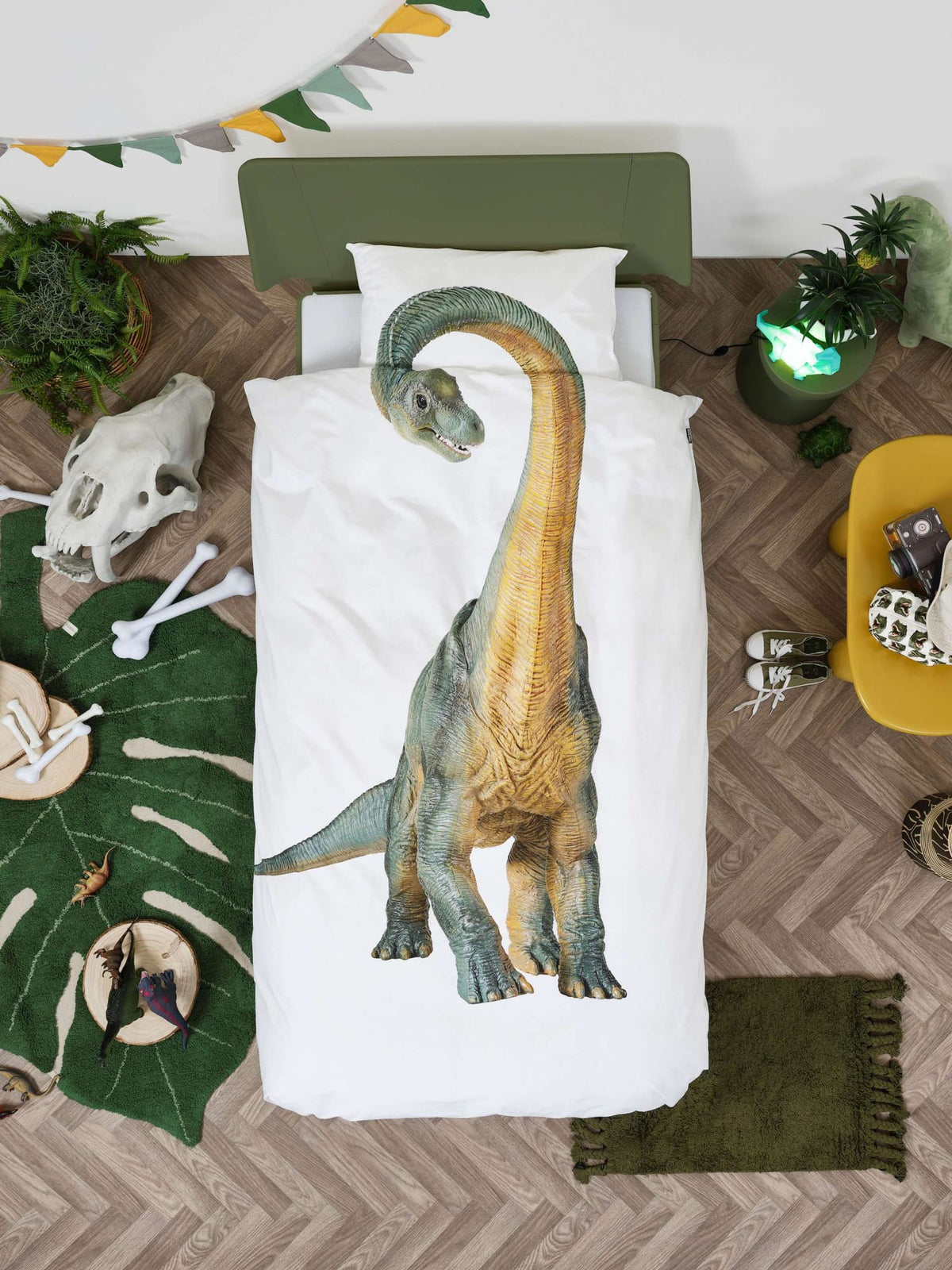 Wit Dino Bronto dekbedovertrek met grote groen-gele dinosaurus op een bed in een slaapkamer met dinothema.