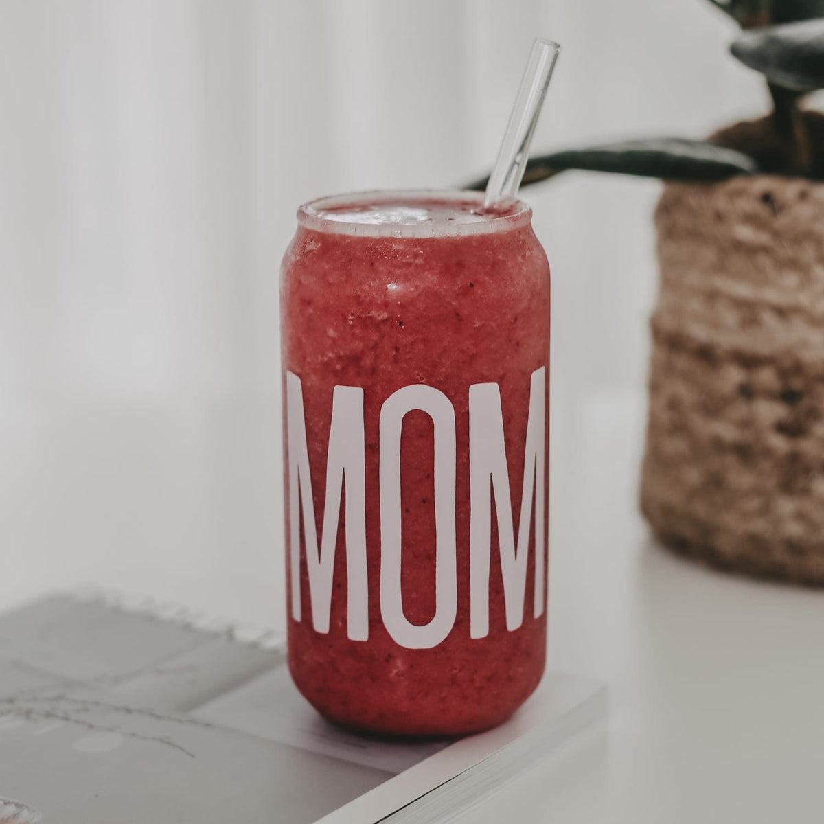 Hoog drinkglas met wit opschrift ‘Mom’, gevuld met een rood drankje en een transparant rietje.