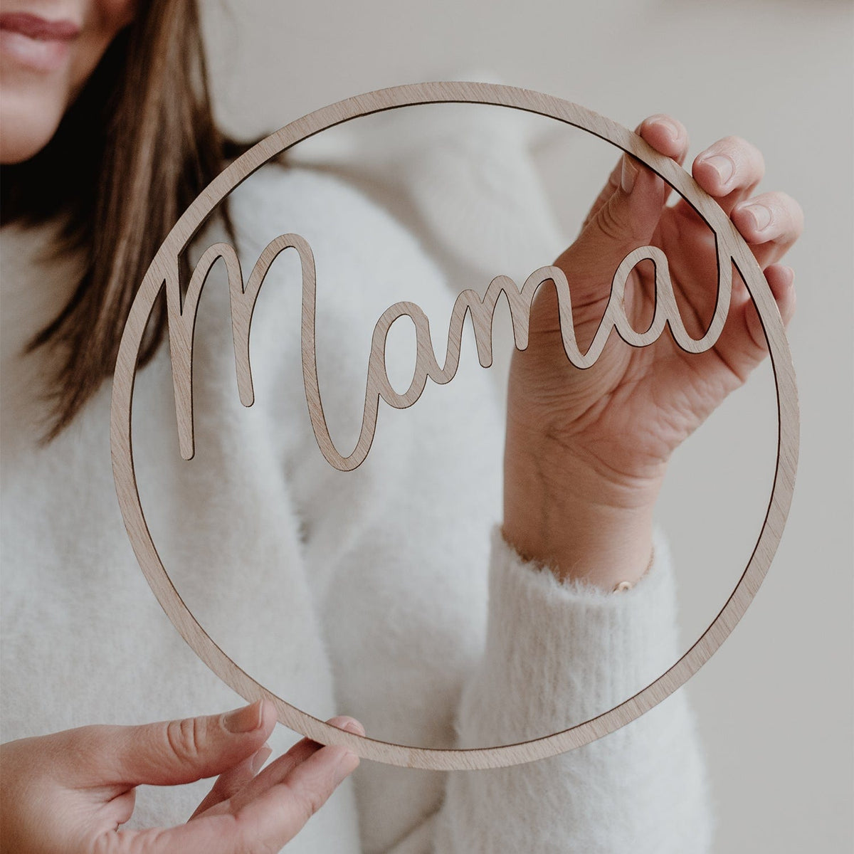 Vrouw houdt een lichtbruine houten krans met het uitgesneden woord mama voor zich.