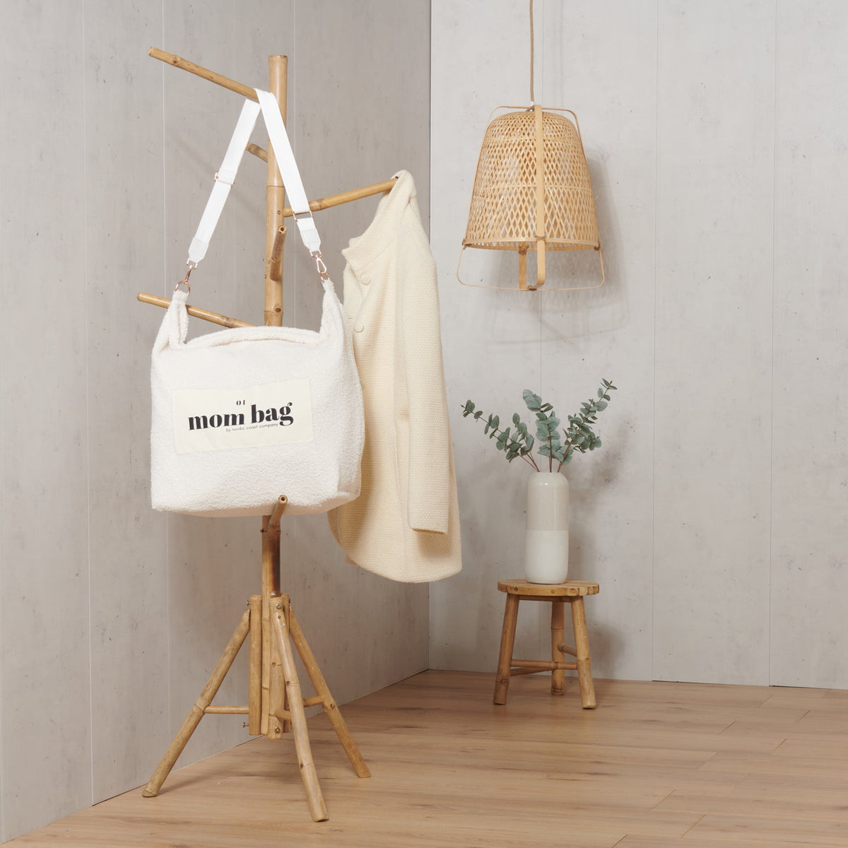 Ivoorkleurige Mom Bag Teddy Bouclé met zwarte opdruk, hangend aan een houten kapstok.