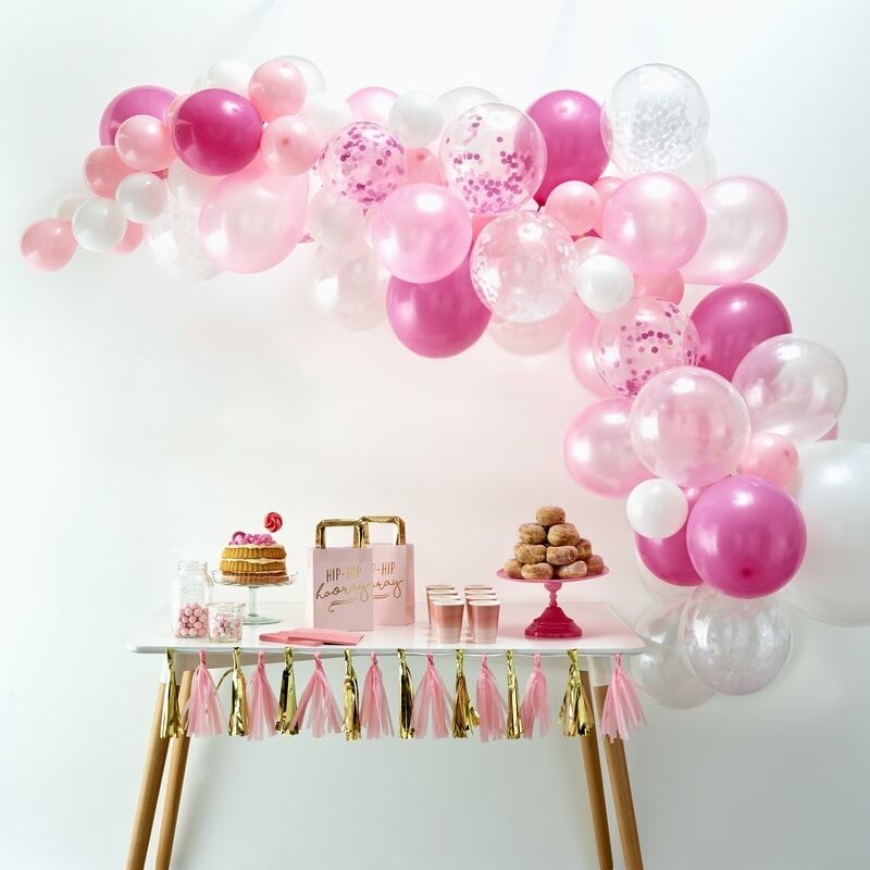 Roze en witte ballonnenboog met confettiballonnen boven een feesttafel met gebak en roze en gouden slingers