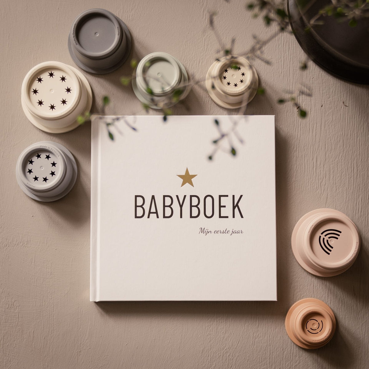 Babyboek mijn eerste jaar op een tafel, omringd door stapelbekers in zachte kleuren.