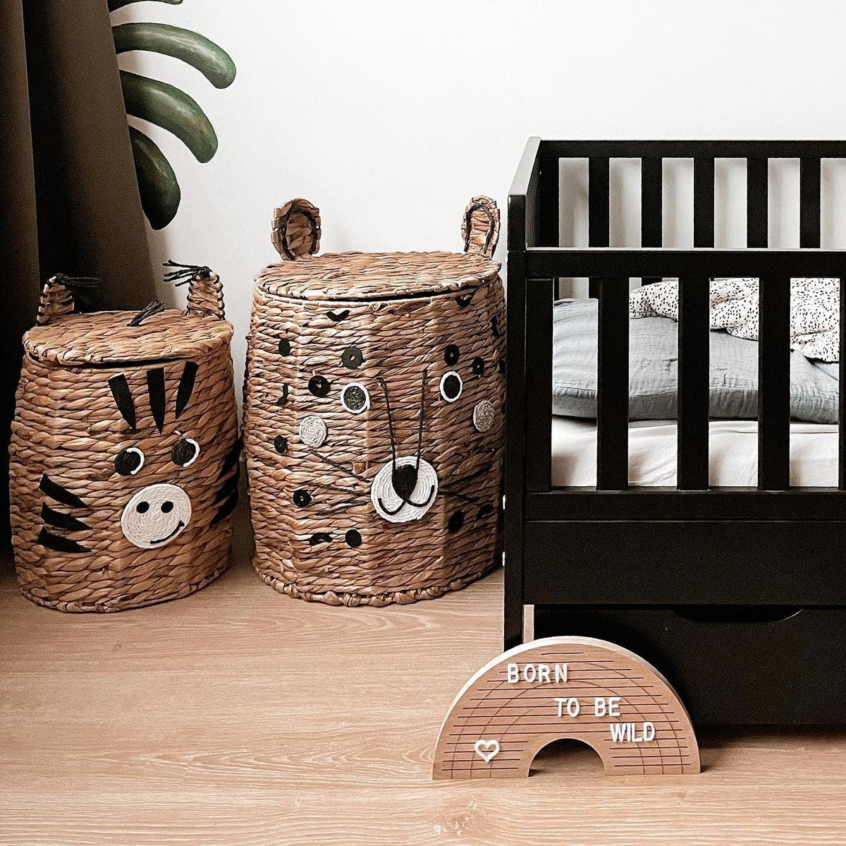Houten regenboogletterbord met 'born to be wild' op de vloer naast een zwart babybed en twee dierenmanden.