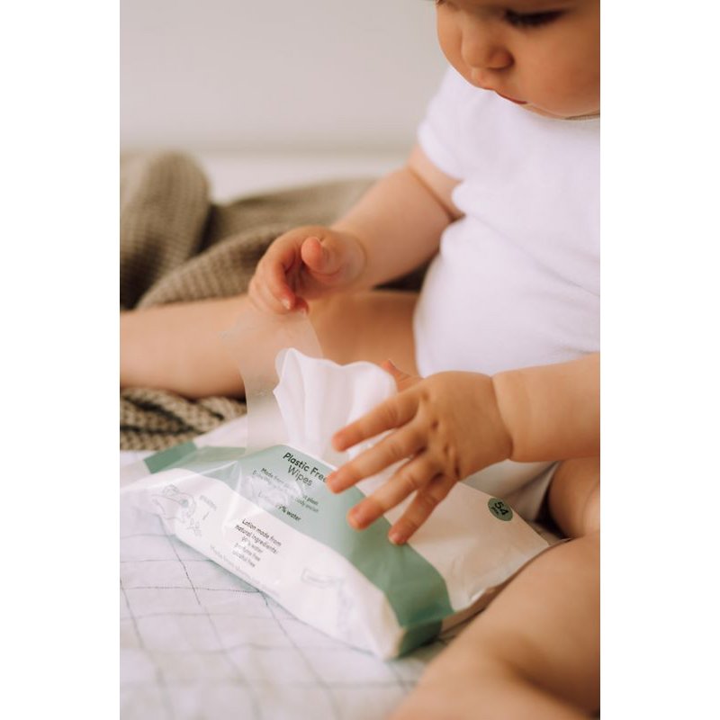Baby in een wit rompertje met een geopend pak Naïf plasticvrije billendoekjes tussen de benen.
