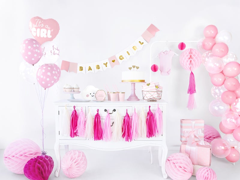 Baby Girl-slinger boven een witte kast met taart en gebakjes, omringd door roze en witte feestdecoratie.