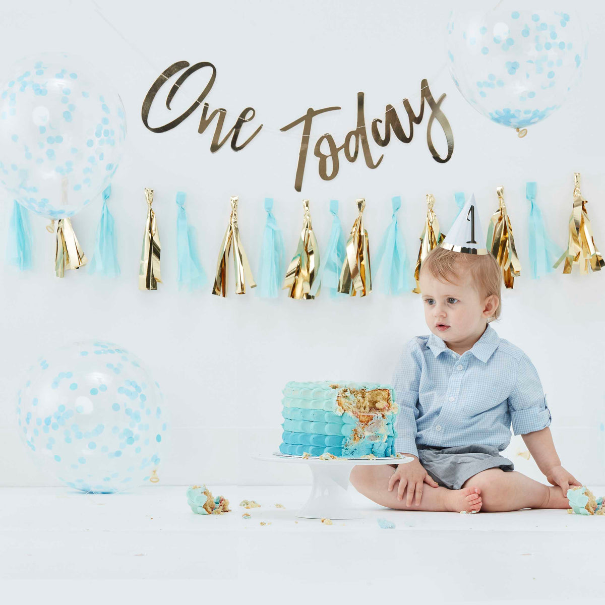 Blauwe cake smash kit met ballonnen en gouden 'One Today'-slinger bij een kind met een blauwe verjaardagstaart.