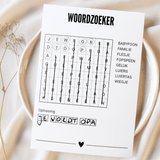 Witte A6-woordzoekerkaart met ingevulde oplossing ‘Je wordt opa’ op een bord met lichte stof en droogbloemen.