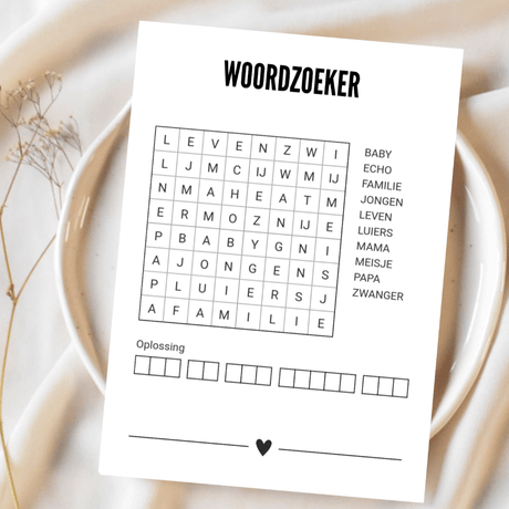 Witte A6-kaart met oningevulde woordzoeker en zwart hartje op een bord met lichte stof en droogbloemen.