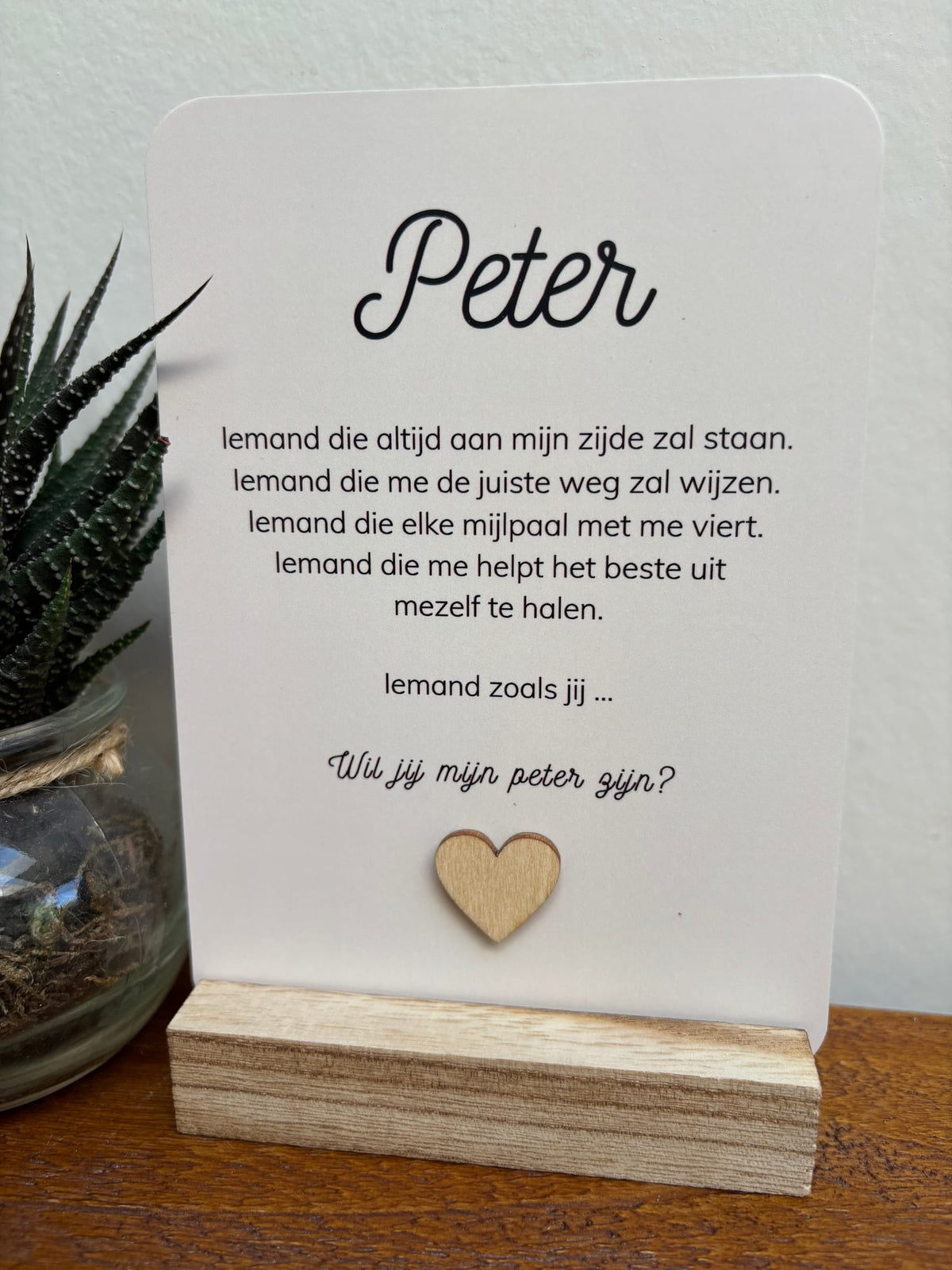 Witte ansichtkaart met ‘Peter’ en ‘Wil jij mijn peter zijn?’, een houten hartje en afgeronde hoeken in een houten houder.
