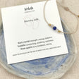 Mommy Milk borstvoedingsarmband met beige koord en gekleurde kralen op een kaartje in een blauw-wit schaaltje.