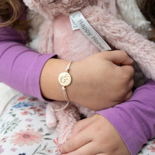 Kind draagt het armbandje met goudkleurige vlinderbedel en houdt een roze knuffel vast.