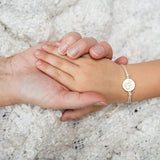 Kinderhand met het lichtroze armbandje met goudkleurige vlinderbedel rust in de hand van een volwassene.