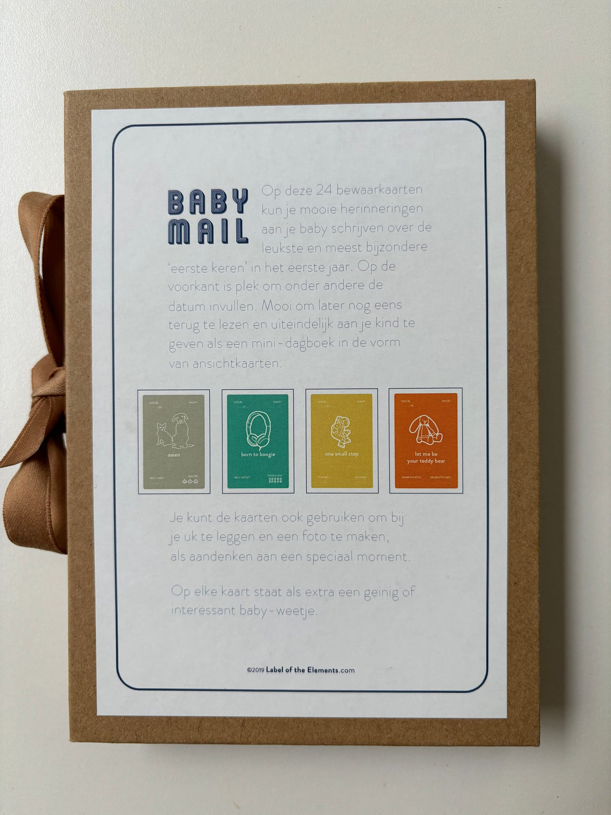 Achterkant van het bruine Baby Mail bewaardoosje met uitleg en voorbeelden van de mijlpaalkaarten.