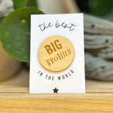 Houten Big Brother badge op een witte kaart met zwarte tekst en een ster, rechtop in een houten houder.