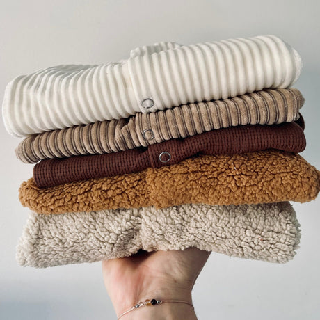 Stapel opgevouwen babykleding op een hand, met het zandkleurige boxpakje Curduroy Sand als tweede van boven.