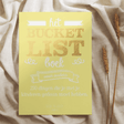 Geel Bucketlist Boek voor ouders op een lichte doek, naast gedroogde graanhalmen.
