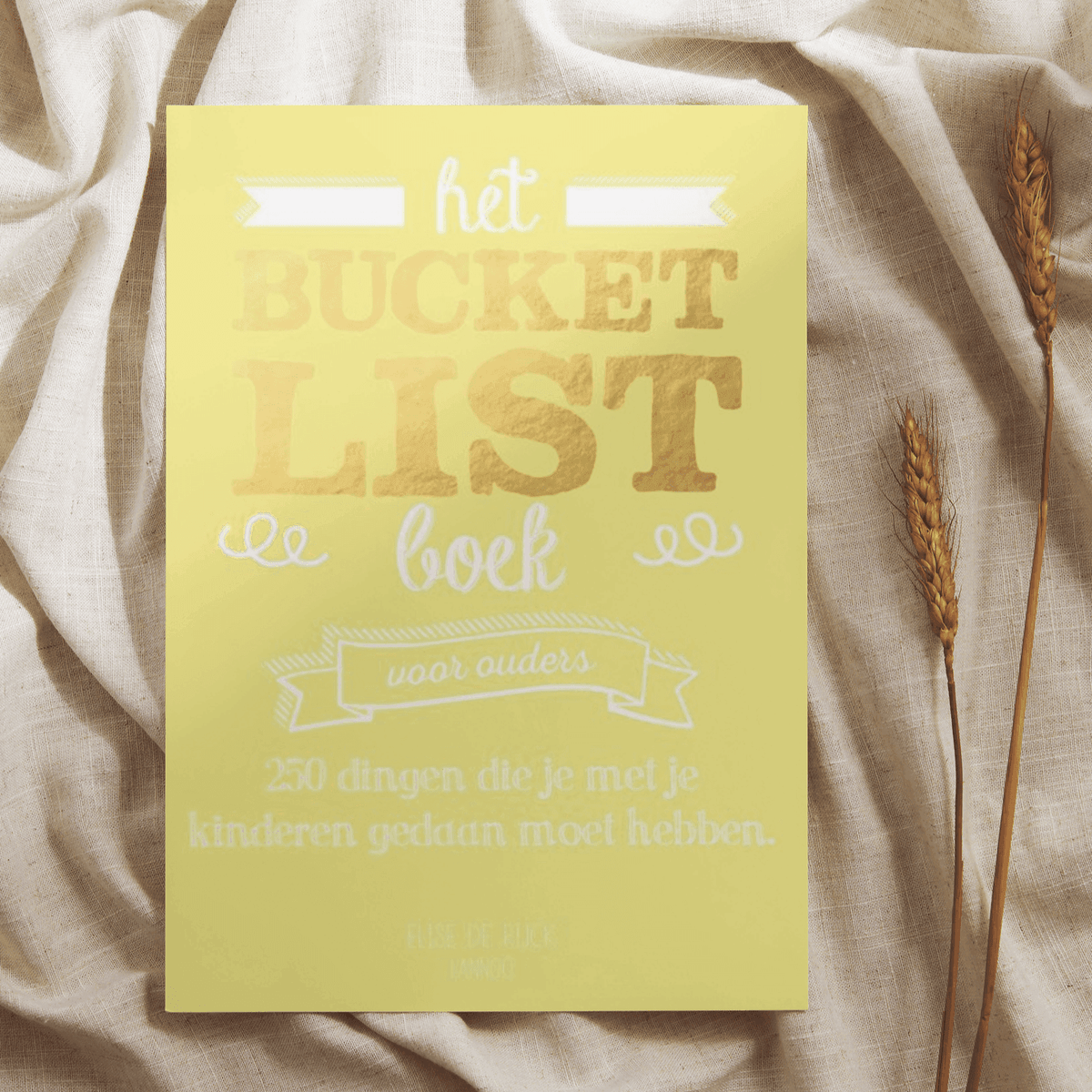 Geel Bucketlist Boek voor ouders op een lichte doek, naast gedroogde graanhalmen.