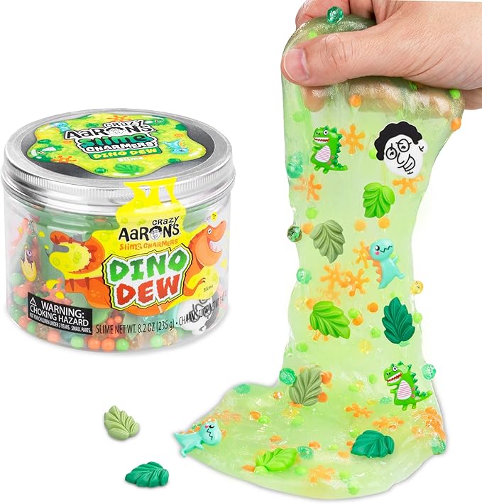 Een hand rekt felgroen Crazy Aaron's Dino Dew-slijm met dinosaurus- en bladbedeltjes uit naast de pot.