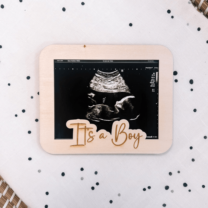 Houten echolijst met echofoto en de tekst 'It's a Boy' op een witte ondergrond met donkere stippen.
