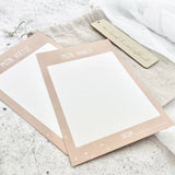 Twee beige kaartjes voor hand- en voetafdrukken met witte afdrukvlakken, naast het linnen bewaarzakje.