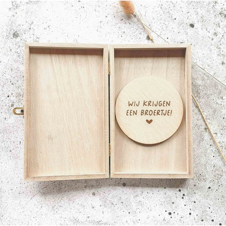 Open houten kistje met een ronde houten schijf met de tekst ‘Wij krijgen een broertje!’ en een hartje.