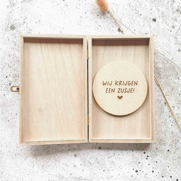 Open houten kistje met een houten cirkel met de tekst ‘Wij krijgen een zusje!’ en een hartje.