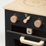 Detail van de zwarte houten speelkeuken met houten knoppen en een geopende ovendeur met houten handgreep.