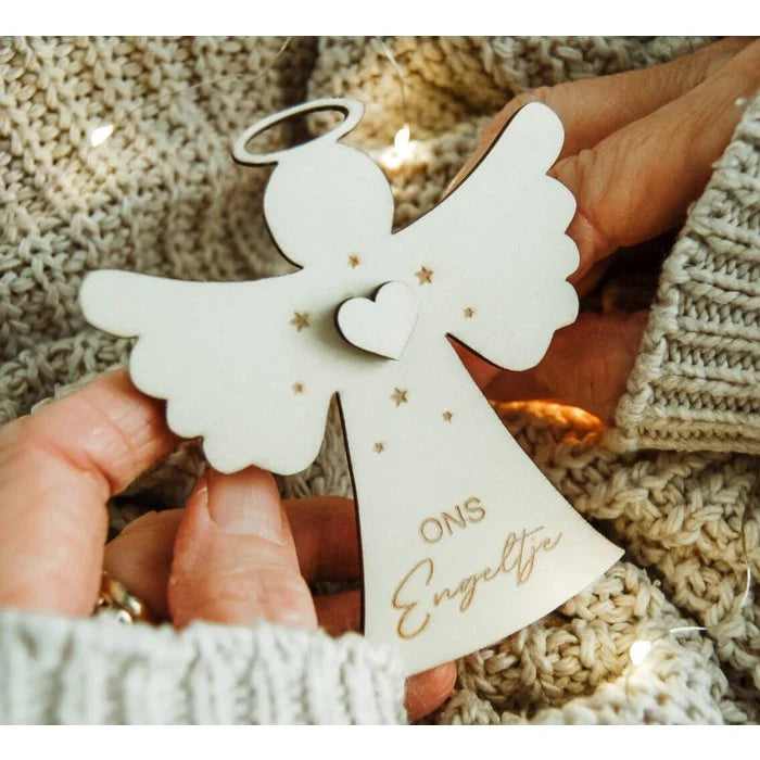 Witte houten kerstengel met hartje, sterren en opschrift ‘Ons Engeltje’, vastgehouden boven een gebreide deken.