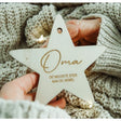 Houten kerstster met ‘Oma, de mooiste ster aan de hemel’, vastgehouden door handen tegen een gebreide achtergrond.