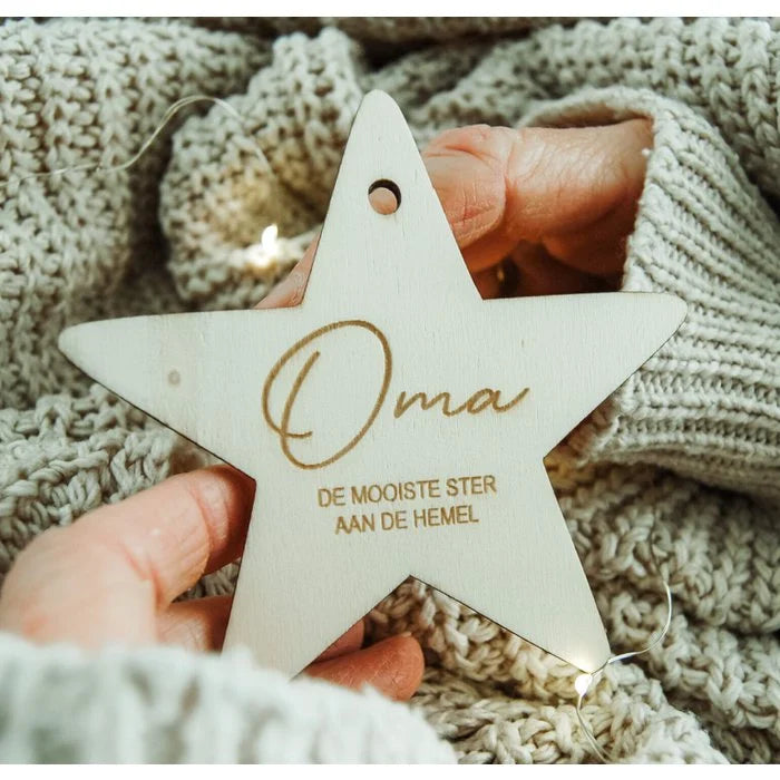Houten kerstster met ‘Oma, de mooiste ster aan de hemel’, vastgehouden door handen tegen een gebreide achtergrond.