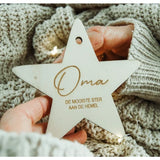 Houten kerstster met ‘Oma, de mooiste ster aan de hemel’, vastgehouden door handen tegen een gebreide achtergrond.