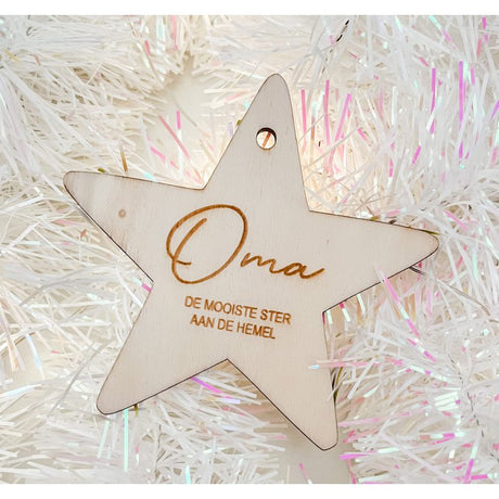Houten kerstster met ‘Oma, de mooiste ster aan de hemel’ tussen witte, glanzende kerstslingers.