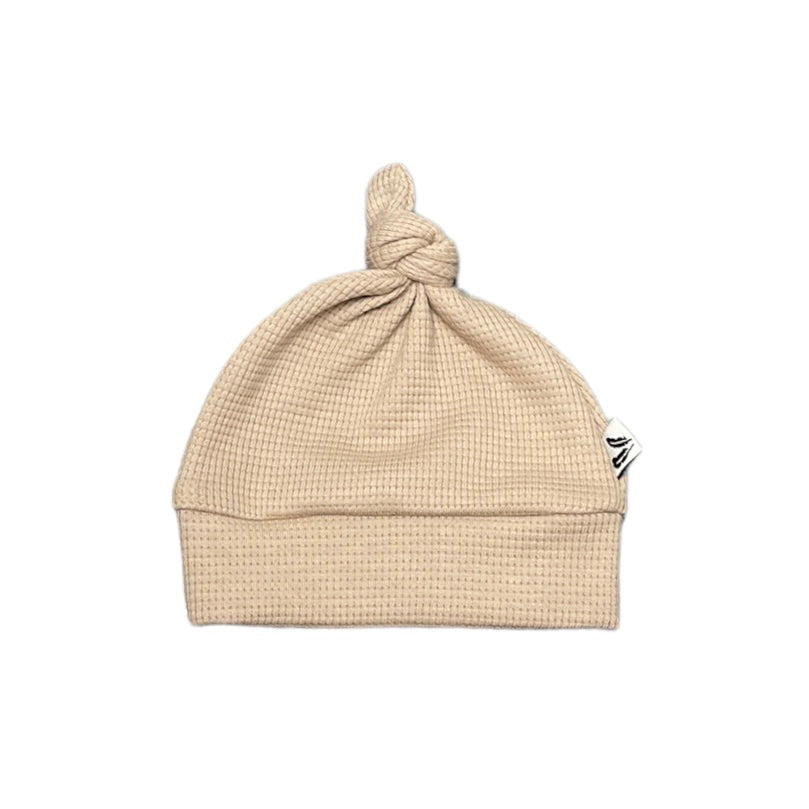 Donkerbeige knoopmutsje met wafelstructuur, omgeslagen rand en een knoop bovenop, op een witte achtergrond.