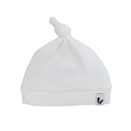 Offwhite knoopmutsje met wafelstructuur, omgeslagen rand en klein label met zwart veertje.