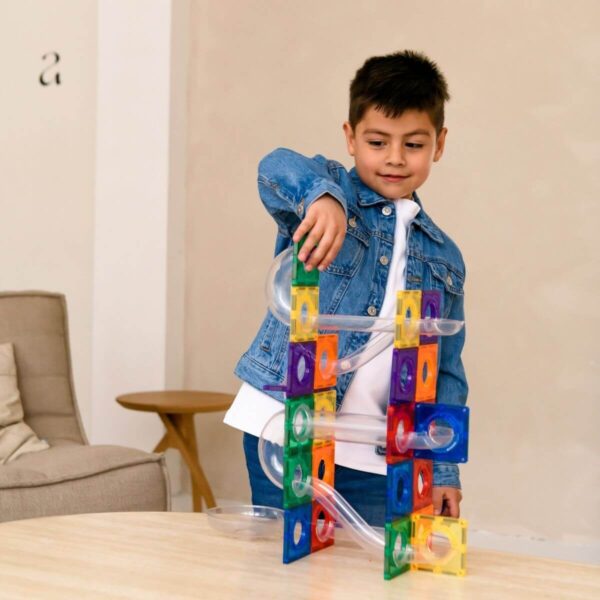 Kind speelt aan tafel met een hoge knikkerbaan van kleurrijke magnetische bouwblokken en doorzichtige buizen