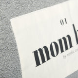 Detail van het lichte etiket met zwarte opdruk op de grijze Mom Bag Teddy Bouclé.