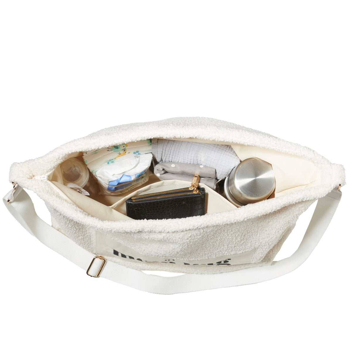 Open Mom Bag Teddy Bouclé in een lichte kleur, gevuld met luiers, een fles, een portemonnee en andere spullen.