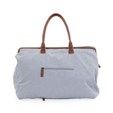 Achterkant van de grijze Mommy Bag verzorgingstas met ritsvak en bruine handvatten.