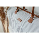 Detail van de grijze Mommy Bag verzorgingstas met bruin merklabel, ritssluiting en bevestiging van de handvatten.
