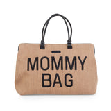 Voorkant van de beige Mommy Bag verzorgingstas met raffialook, zwarte letters en zwarte handvatten.
