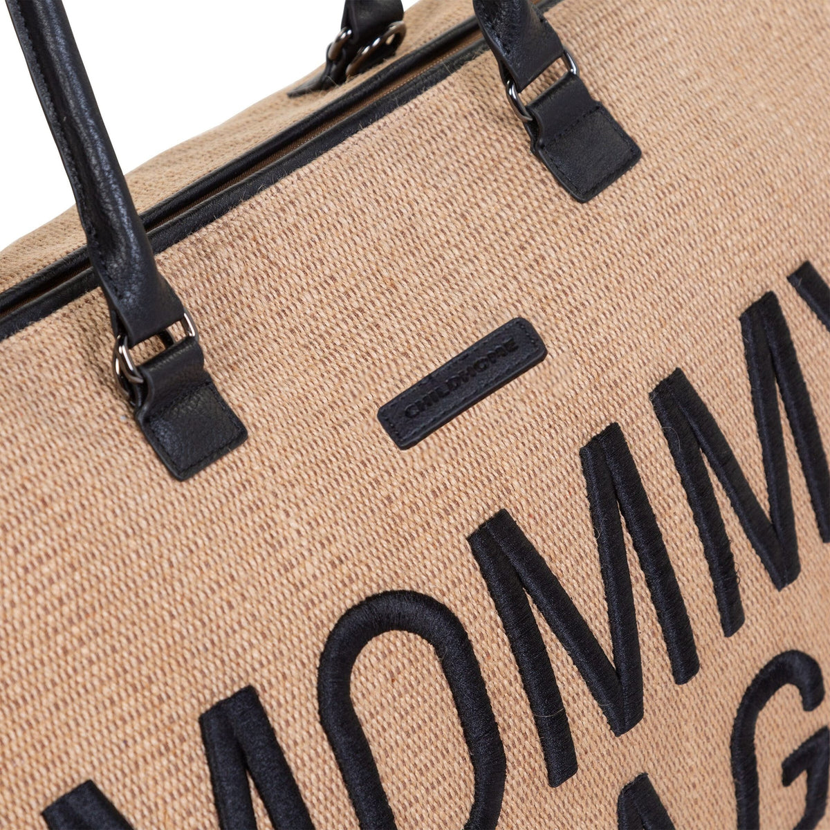 Detail van de beige Mommy Bag verzorgingstas met raffialook, zwarte letters, handvatten en ritssluiting.