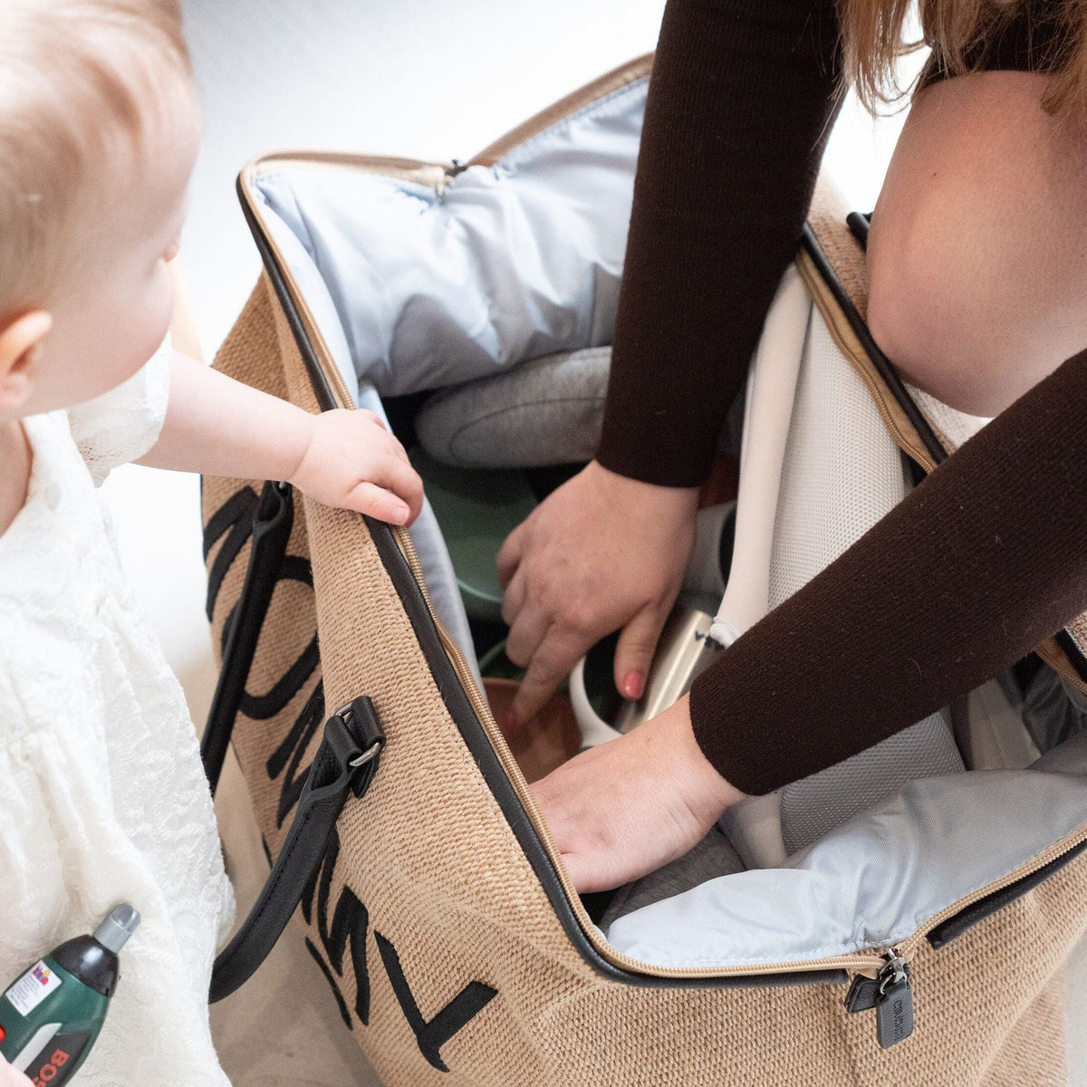 Zwangere vrouw pakt een open Mommy Bag verzorgingstas met grijze binnenkant in, terwijl een kind meekijkt.