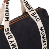 Close-up van de zwarte Mommy Bag verzorgingstas met brede crèmekleurige banden en bruine details.