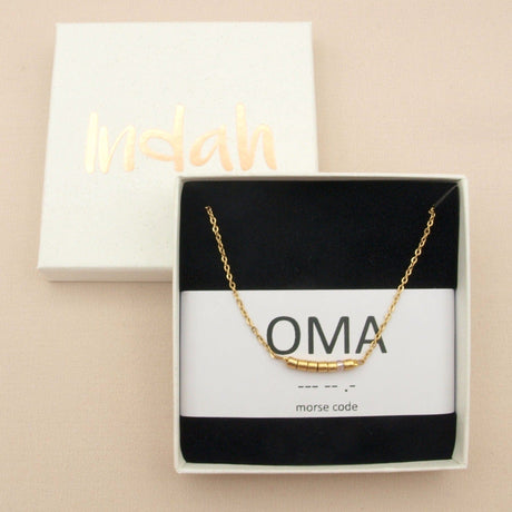 Goudkleurige oma-ketting met morsecodekralen in een open cadeaudoosje, op een kaartje met de tekst ‘oma’.