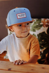 Kind met de blauwe Mini Jean pet van Hello Hossy met bruine klep, schuin van voren gezien.