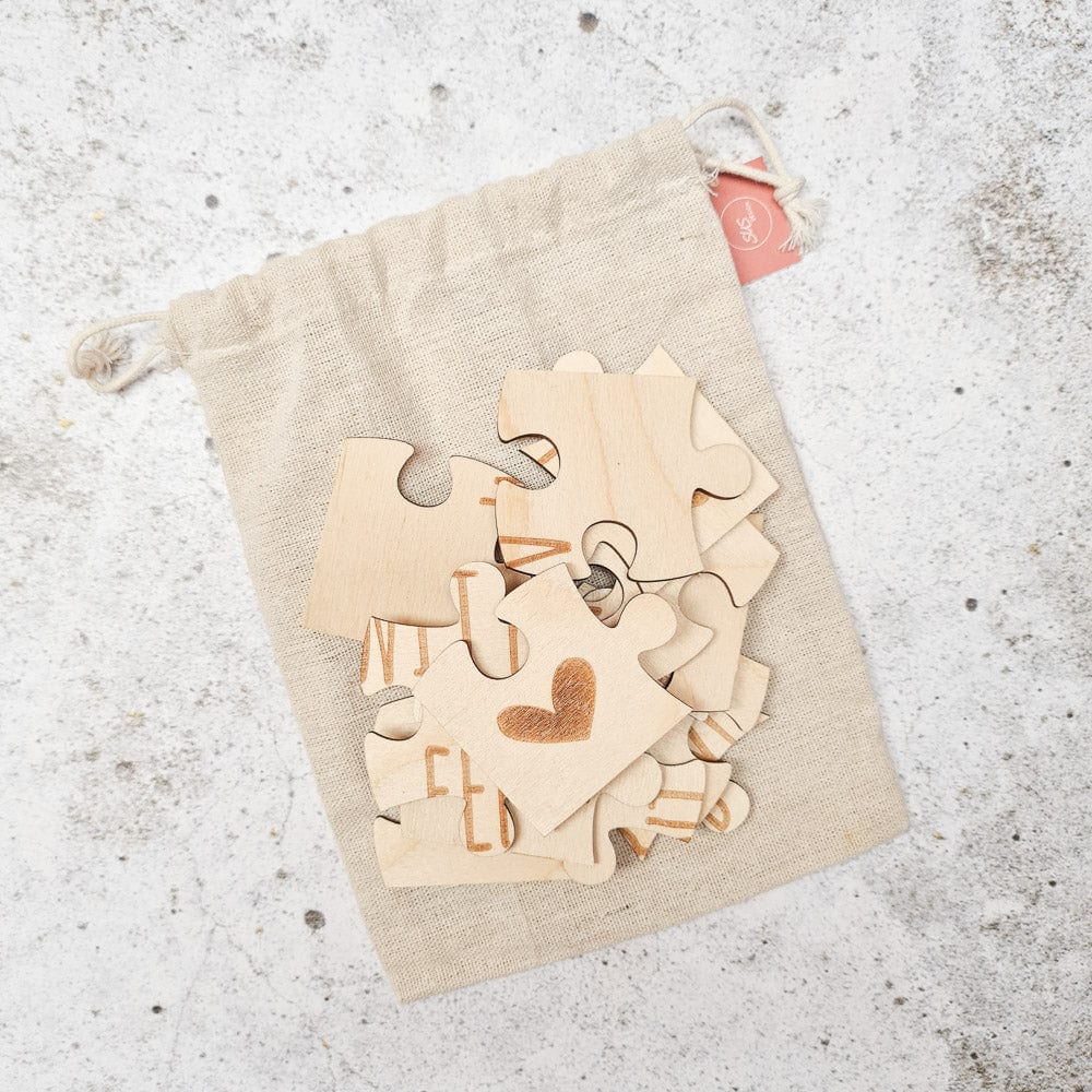 Losse houten stukjes van de puzzel ‘Je wordt tante’ op een beige linnen zakje, met een hartje op één stukje.