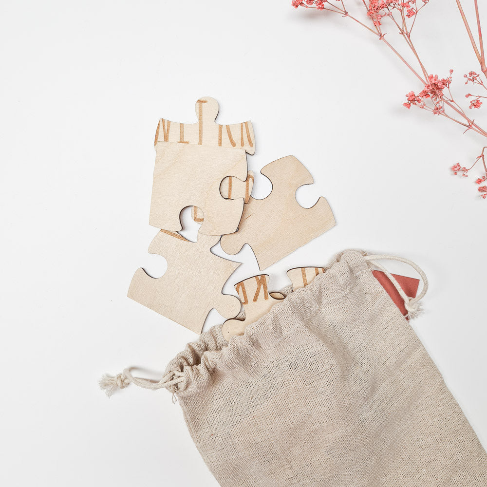 Houten stukjes van de puzzel ‘Je wordt oma’ naast een open beige linnen zakje, met roze bloemetjes.