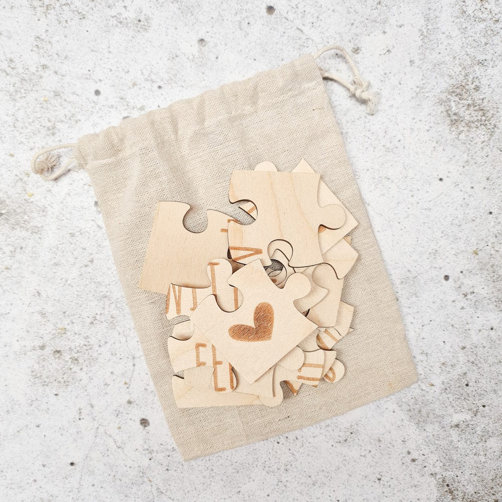 Houten stukjes van de puzzel ‘Je wordt oma’ op een beige linnen zakje, met een hartje op het bovenste stukje.