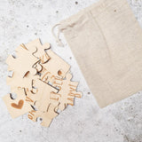Losse houten stukjes van de puzzel ‘Je wordt oma’ met letters en een hartje naast een beige linnen zakje.